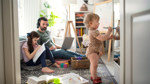 Busy father working with small daughters in bedroom, home office concept.