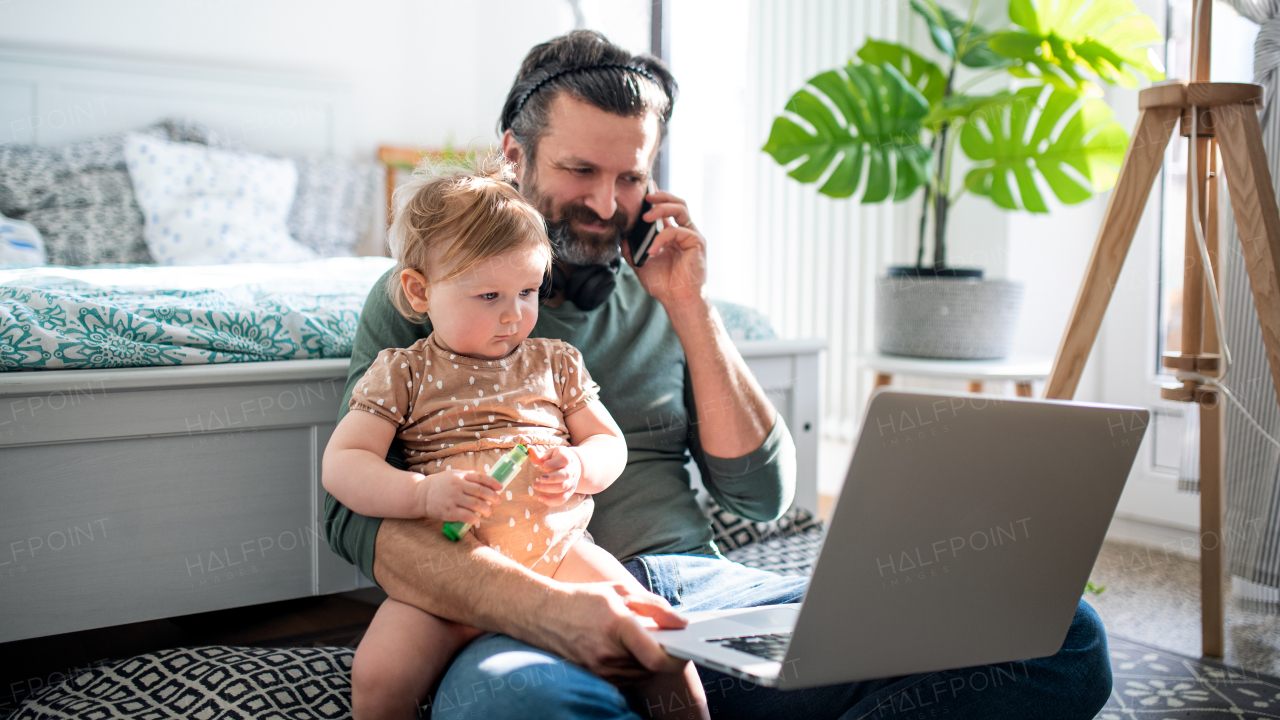 Busy father working with small toddler daughter in bedroom, home office concept.