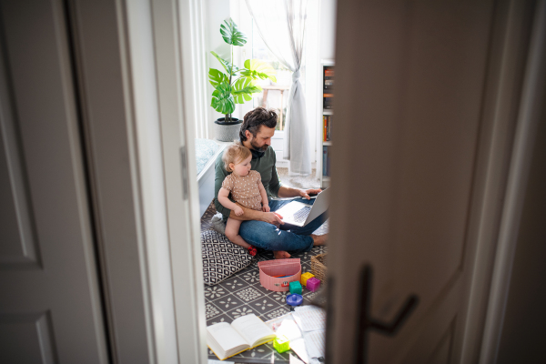 Busy father working with small toddler daughter in bedroom, home office concept.