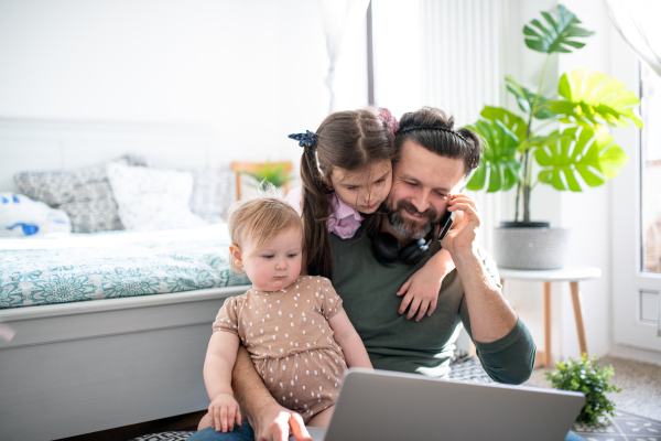 Busy father working with small daughters in bedroom, home office concept.