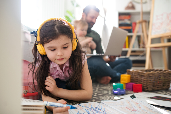 Busy father working with small daughters in bedroom, home office and distance learning concept.