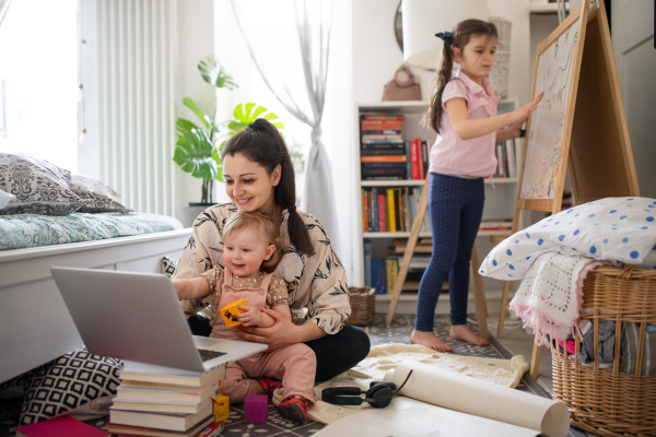 Mother working with two small daughters in bedroom, home office concept.