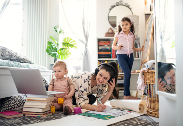 Mother working with two small daughters in bedroom, home office concept.