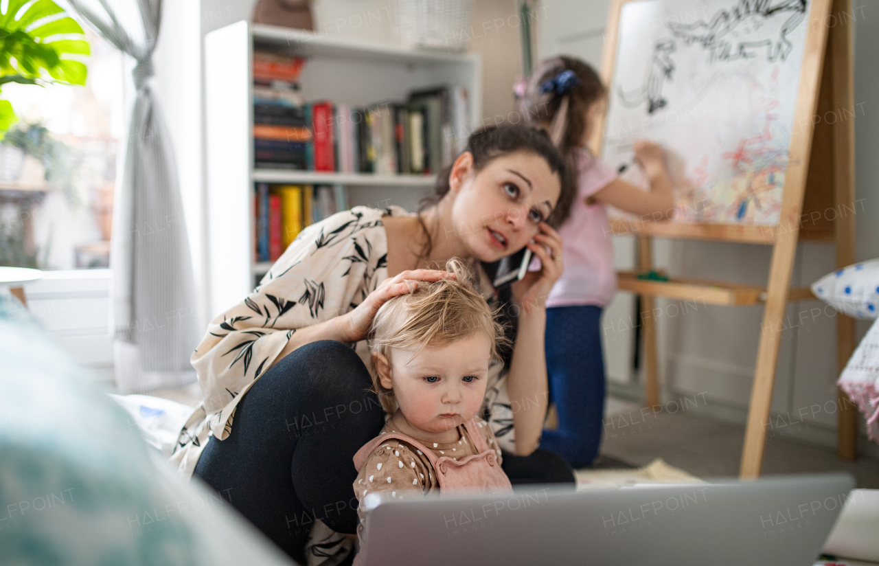 Mother working with two small daughters in bedroom, home office concept.