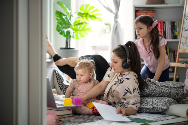 Mother working with two small daughters in bedroom, home office concept.