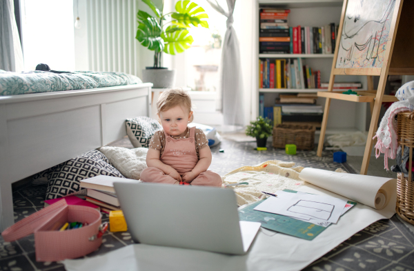 A small toddler girl on floor at home, watching story tales on laptop.