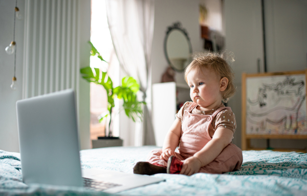 Small toddler girl on bed at home, watching story tales on laptop.