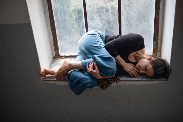 Portrait of lonely woman lying on old and dirty window sill, solitude, mental health and depression concept.