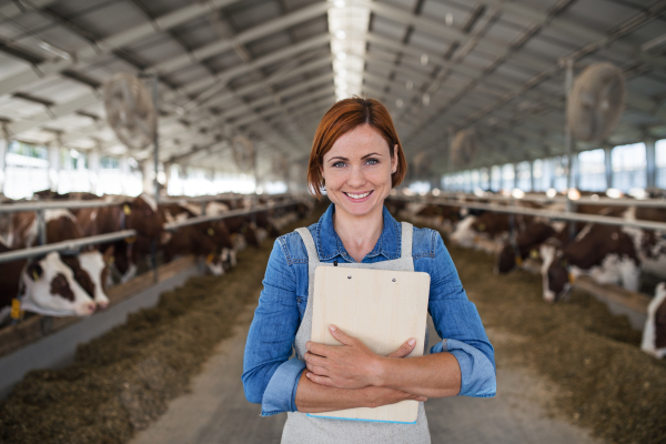 Woman manager with clipboard standing on diary farm, agriculture industry.