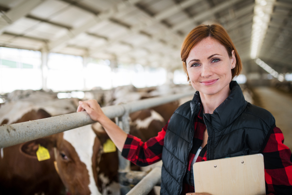 Woman manager with clipboard standing on diary farm, agriculture industry. Copy space.