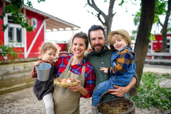 Portrait of happy family with small children standing on farm, holding basket with eggs.