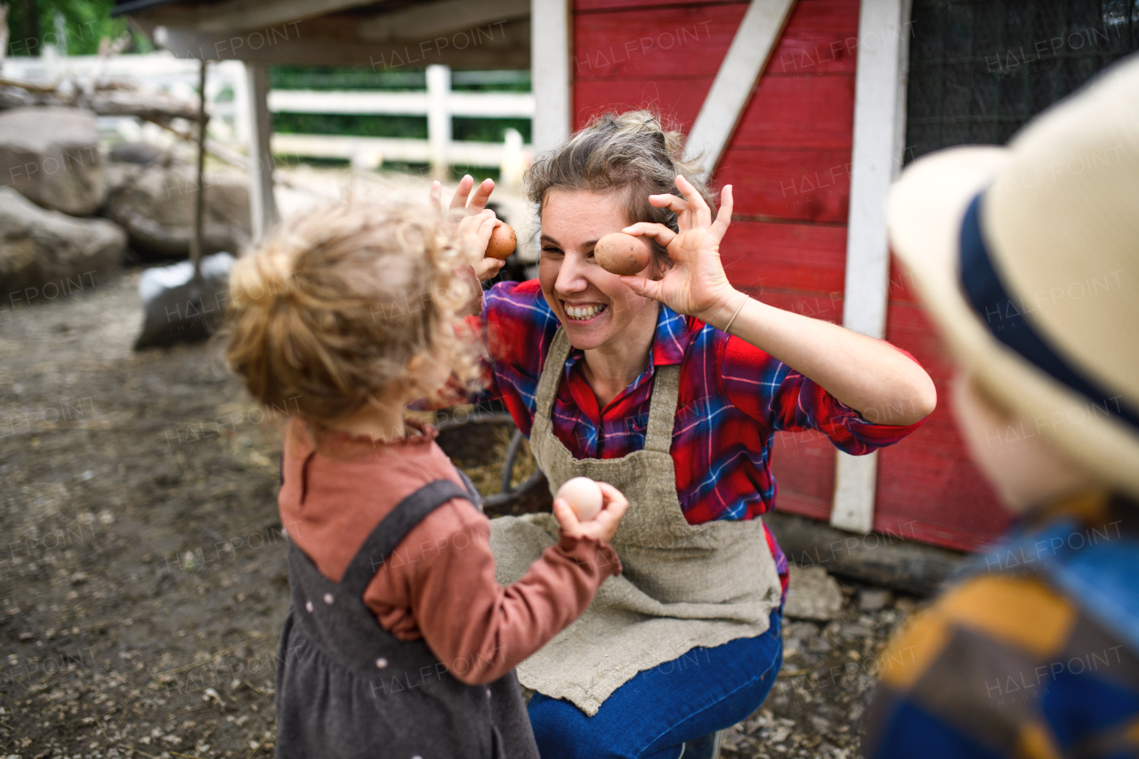 Cheerful mother with small children standing on farm, having fun when collecting eggs.