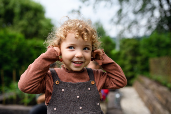 Portrait of cute small girl standing on farm, holding cherry earrings.