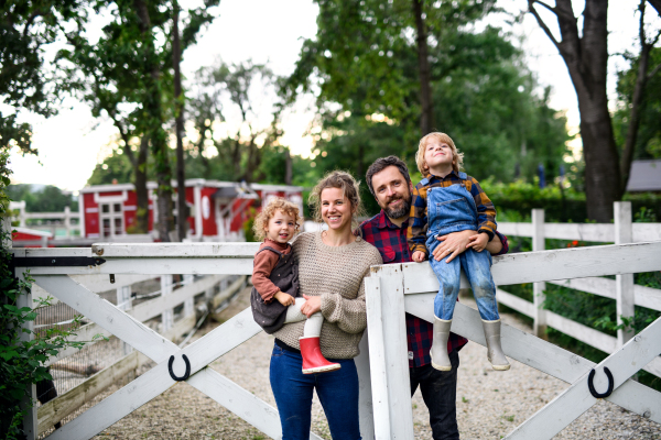 Portrait of happy family with small children standing on farm.