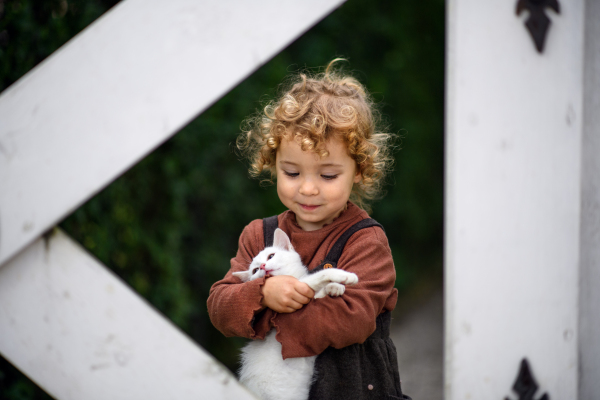 Portrait of cute small girl standing on farm, holding cat.