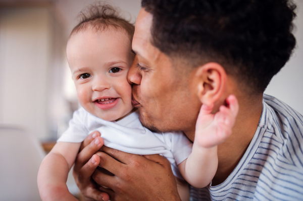 A portrait of cheerful father and small toddler son indoors at home, kissing.