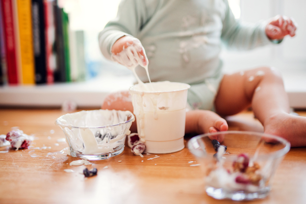 A midsection of small messy toddler boy sitting on kitchen counter at home, eating fruit and yoghurt.