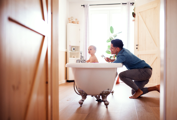 Hispanic father washing small toddler son in a bathroom indoors at home.