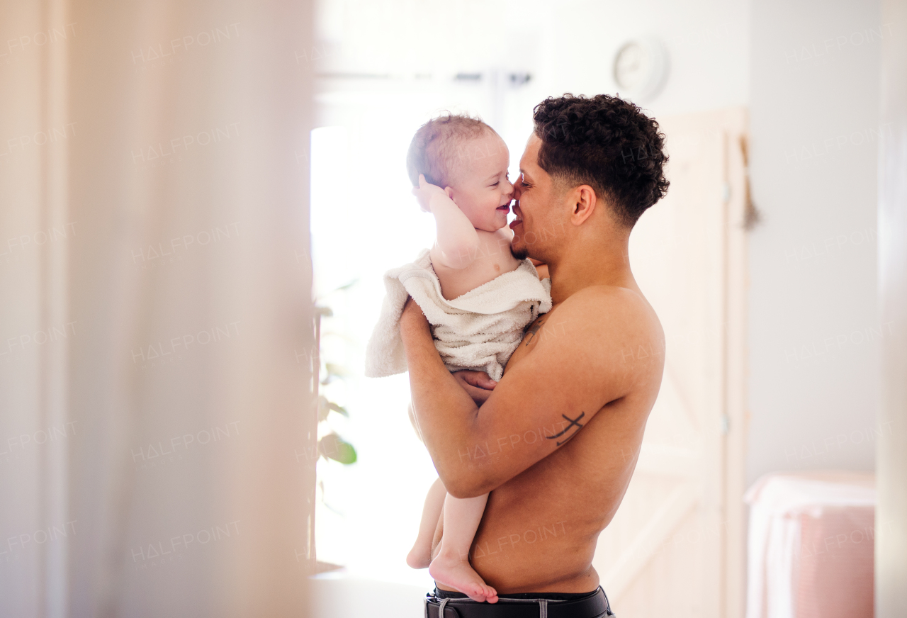 Topless father and small toddler son wrapped in towel in a bathroom indoors at home.