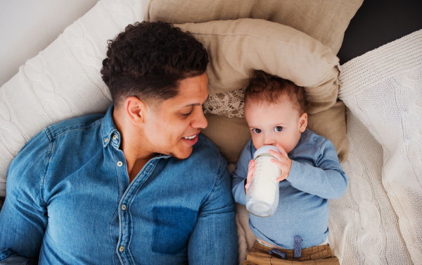 A top view portrait of father and a small toddler son indoors at home, drinking milk from bottle.