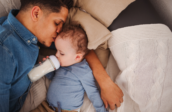 A top view portrait of father and a small toddler son indoors at home, drinking milk from bottle.