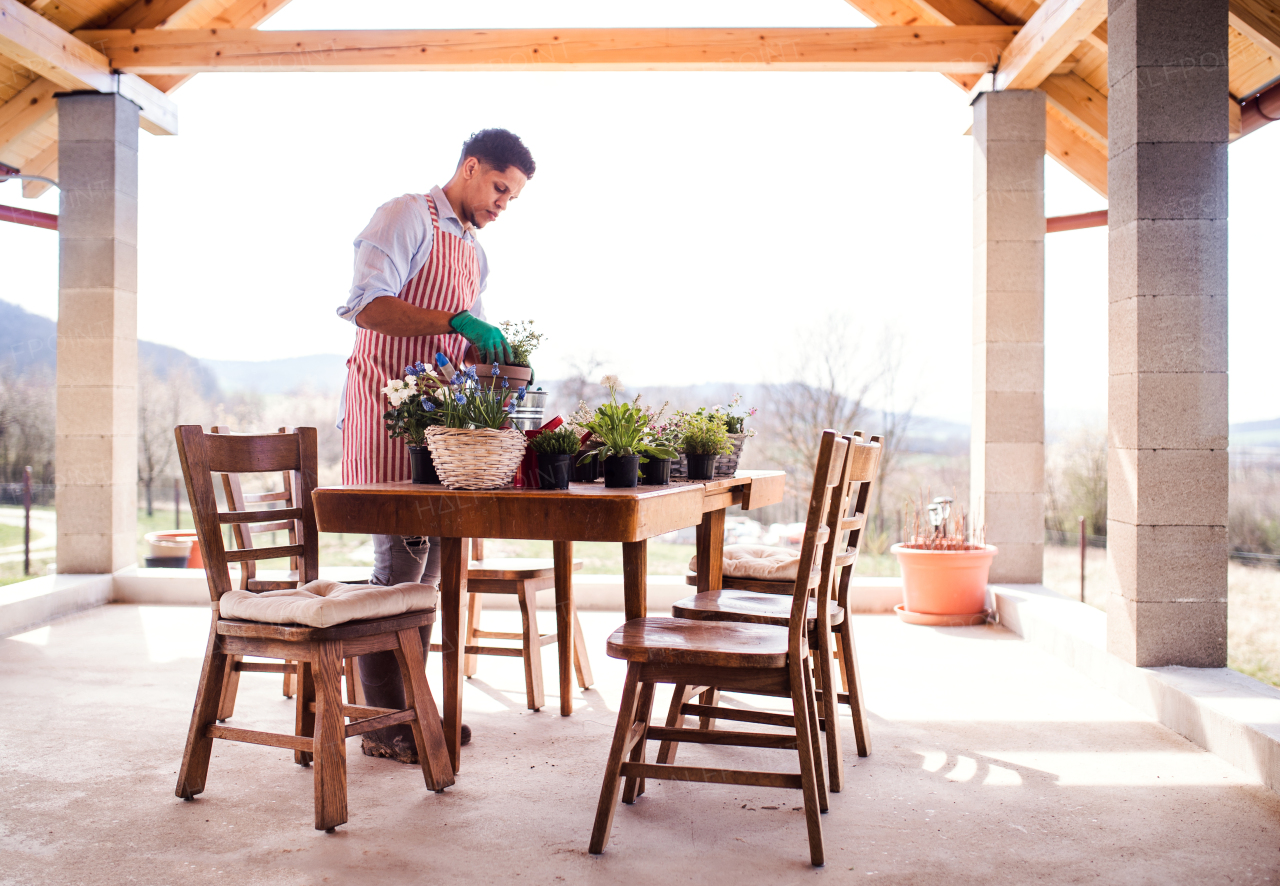 A portrait of young cheerful man gardener outdoors at home, planting flowers.