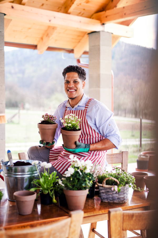 A portrait of young cheerful man gardener outdoors at home, planting flowers.