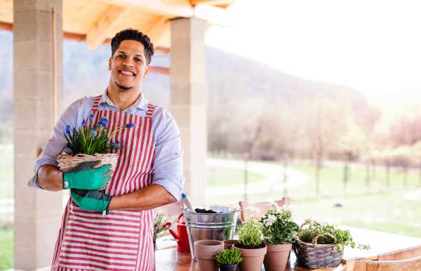 A portrait of young cheerful man gardener outdoors at home, planting flowers.