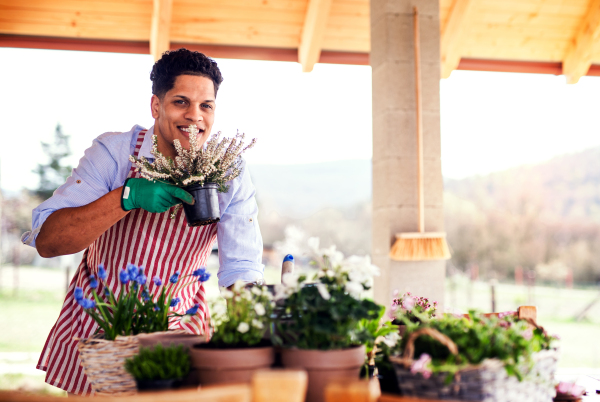 A portrait of young cheerful man gardener outdoors at home, planting flowers.