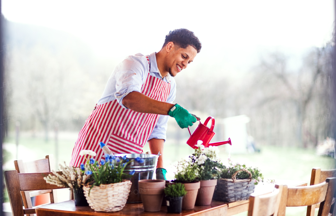 A portrait of young cheerful man gardener outdoors at home, planting flowers.