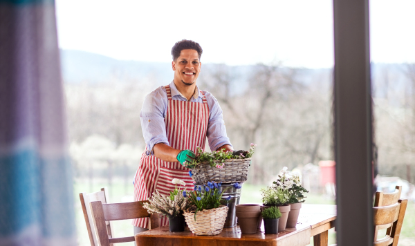 A portrait of young cheerful man gardener outdoors at home, planting flowers.