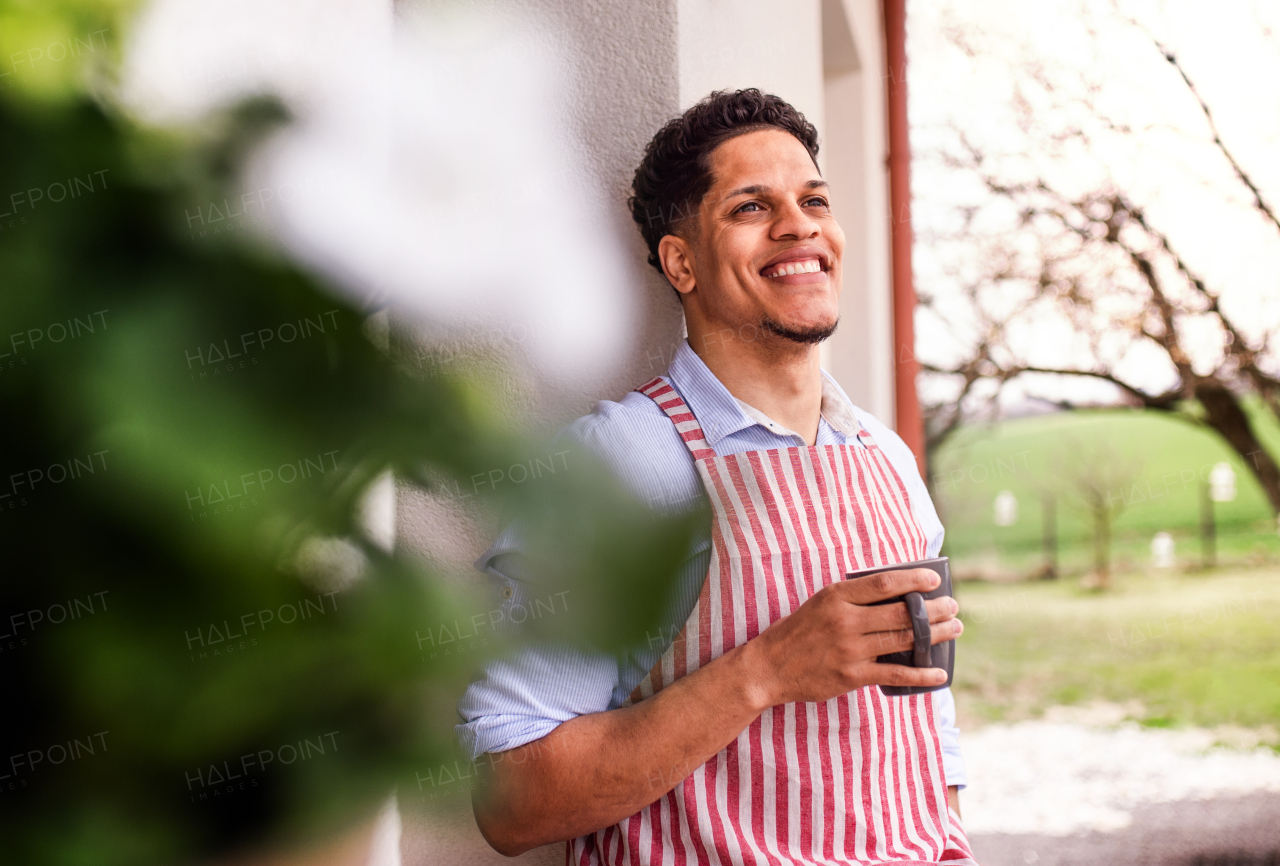 A portrait of young cheerful man gardener outdoors at home, holding a cup of coffee.