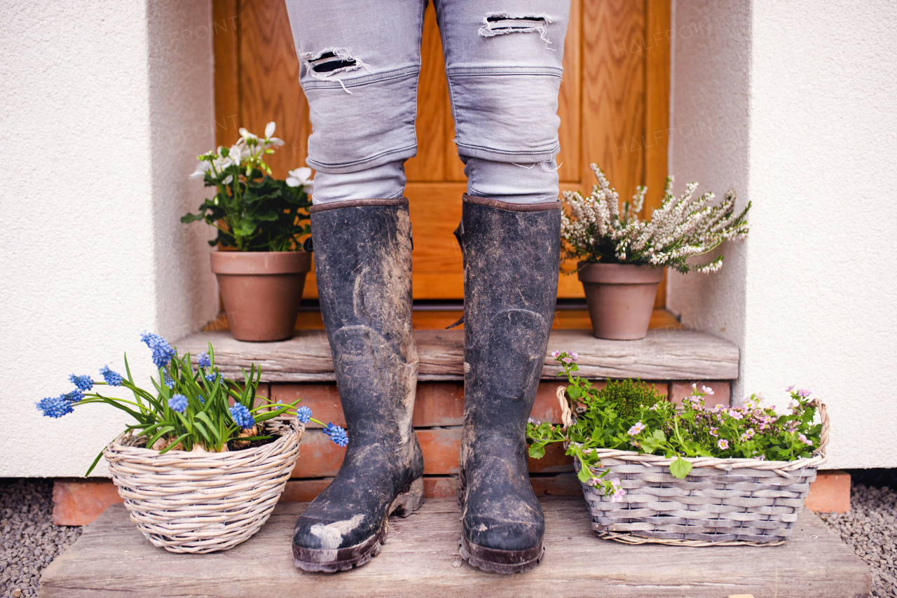 A midsection of young man gardener standing in front of door at home, wearing dirty rubber boots.