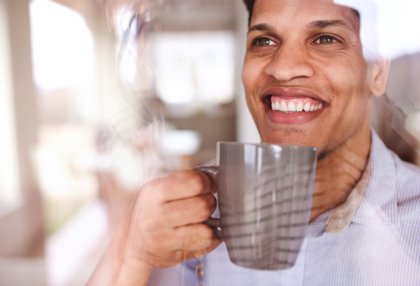 Portrait of hispanic man with a glass of water indoors at home, looking out of window. Shot through glass.