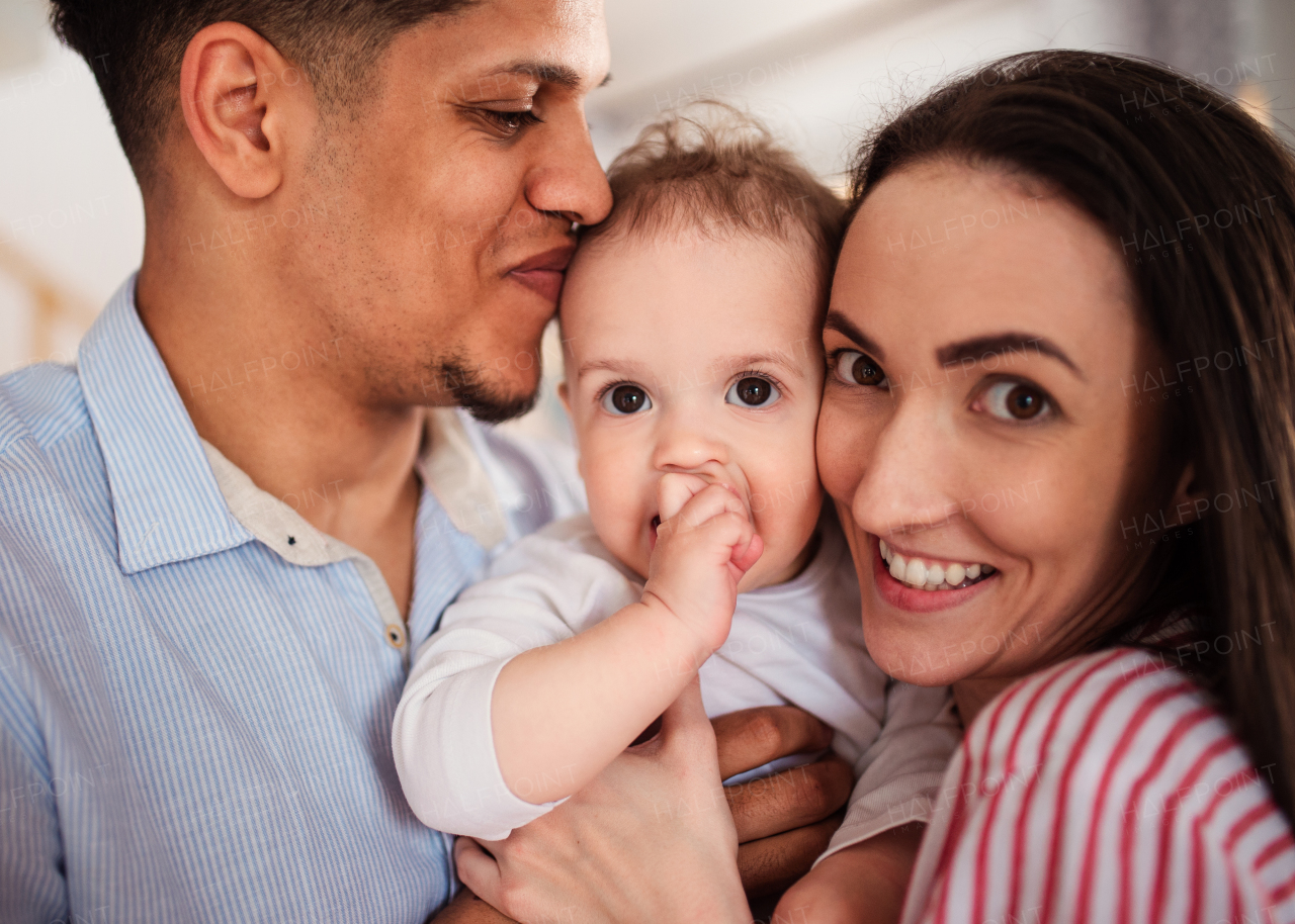 A portrait of young family with small toddler son indoors at home, kissing.