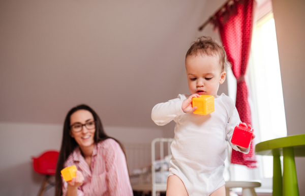 A young mother with small toddler son indoors at home, playing with blocks.