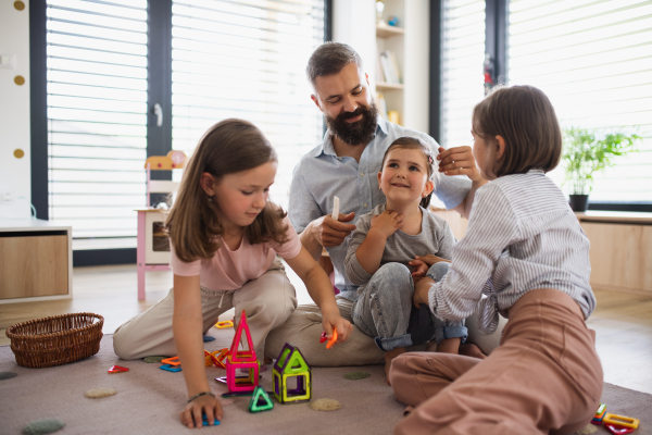 A father with three daughters indoors at home, playing on floor.