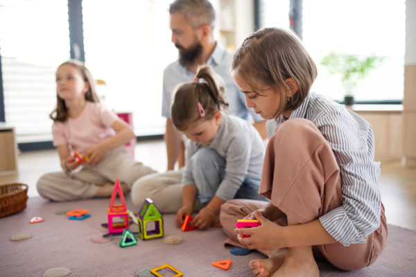 A father with three daughters indoors at home, playing on floor.