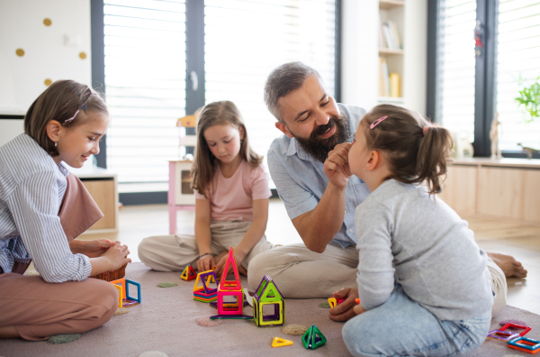 A father with three daughters indoors at home, playing on floor.