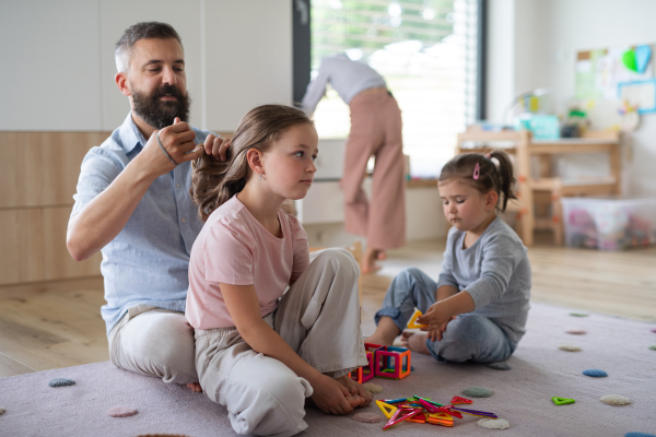 A father with three daughters indoors at home, playing and making hair.