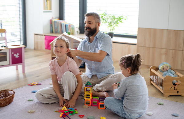 A father with three daughters indoors at home, playing and making hair.