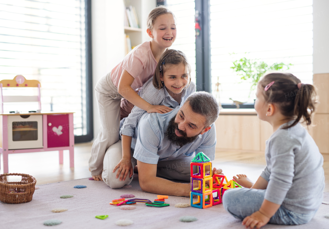 A father with three daughters indoors at home, playing on floor.