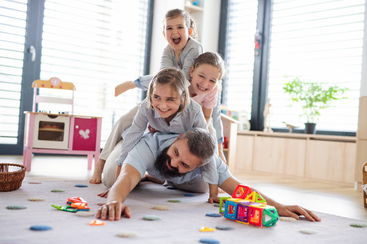 A father with three daughters indoors at home, playing on floor.