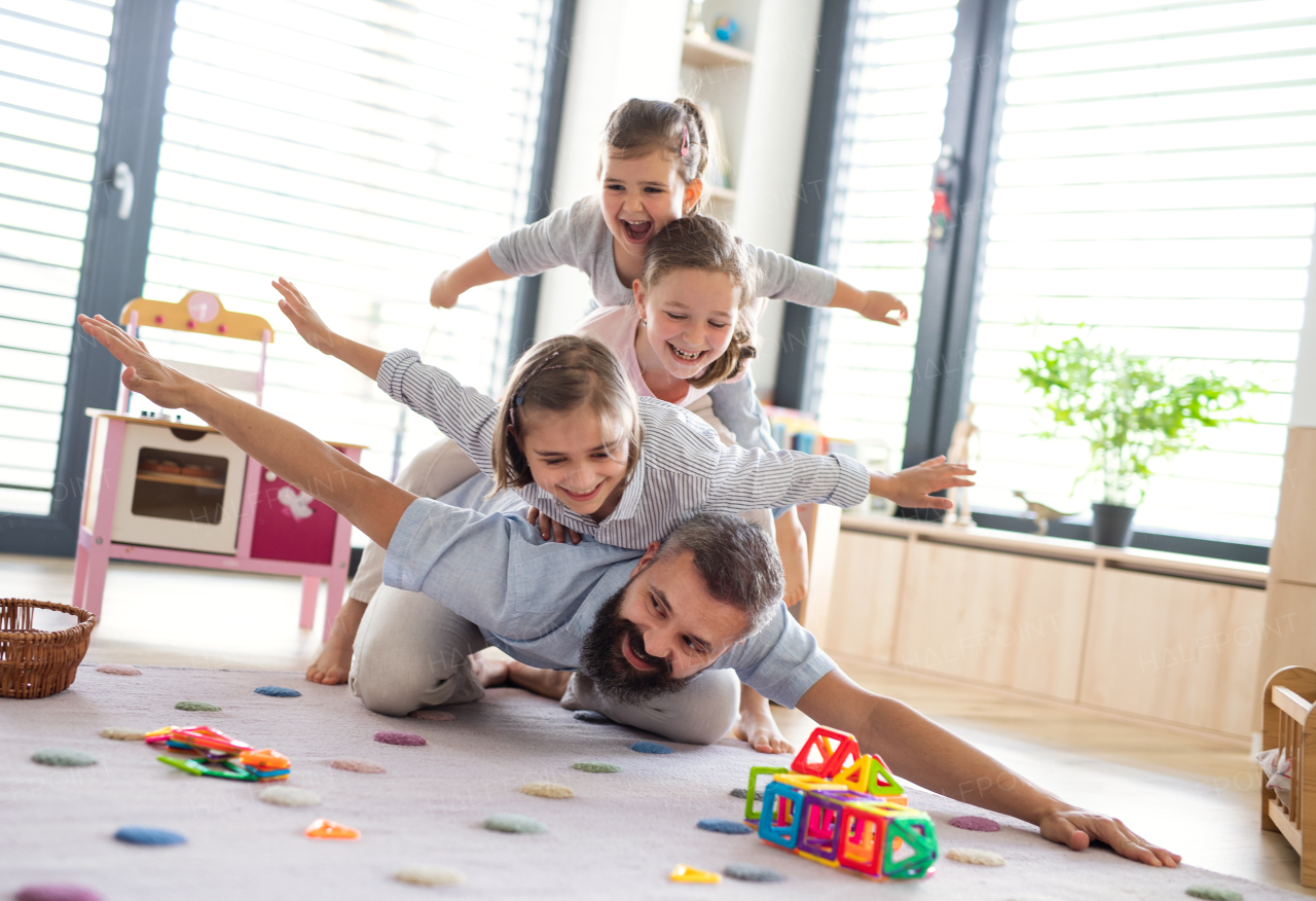 A father with three daughters indoors at home, playing on floor.