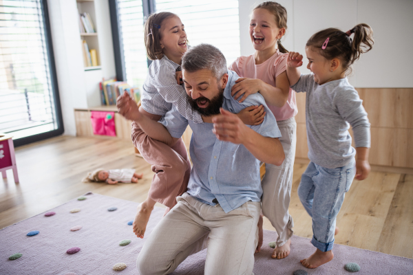 A father with three daughters indoors at home, playing on floor.