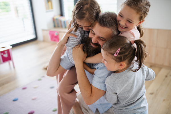 A father with three daughters indoors at home, looking at camera.