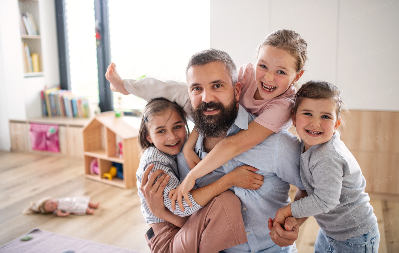 A father with three daughters indoors at home, looking at camera.