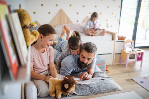 A father with three daughters indoors at home, reading a book.