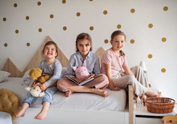 A portrait of three girls sisters indoors at home, looking at camera.