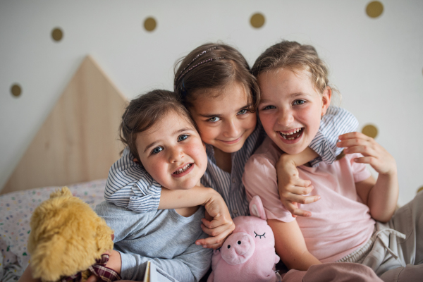 A portrait of three girls sisters indoors at home, looking at camera.